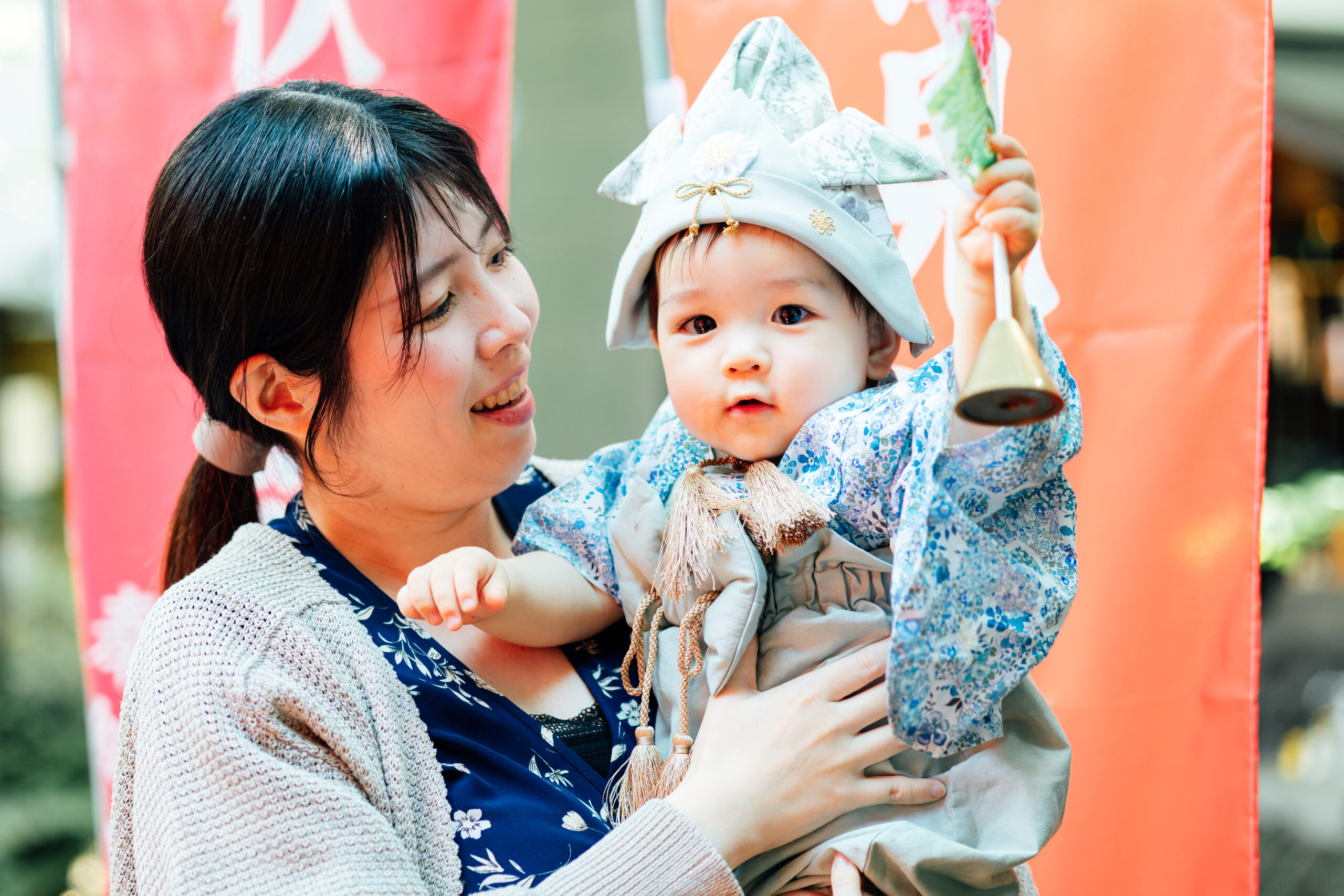 お母さまに抱かれて鈴を持つ、初節句の衣装の赤ちゃん