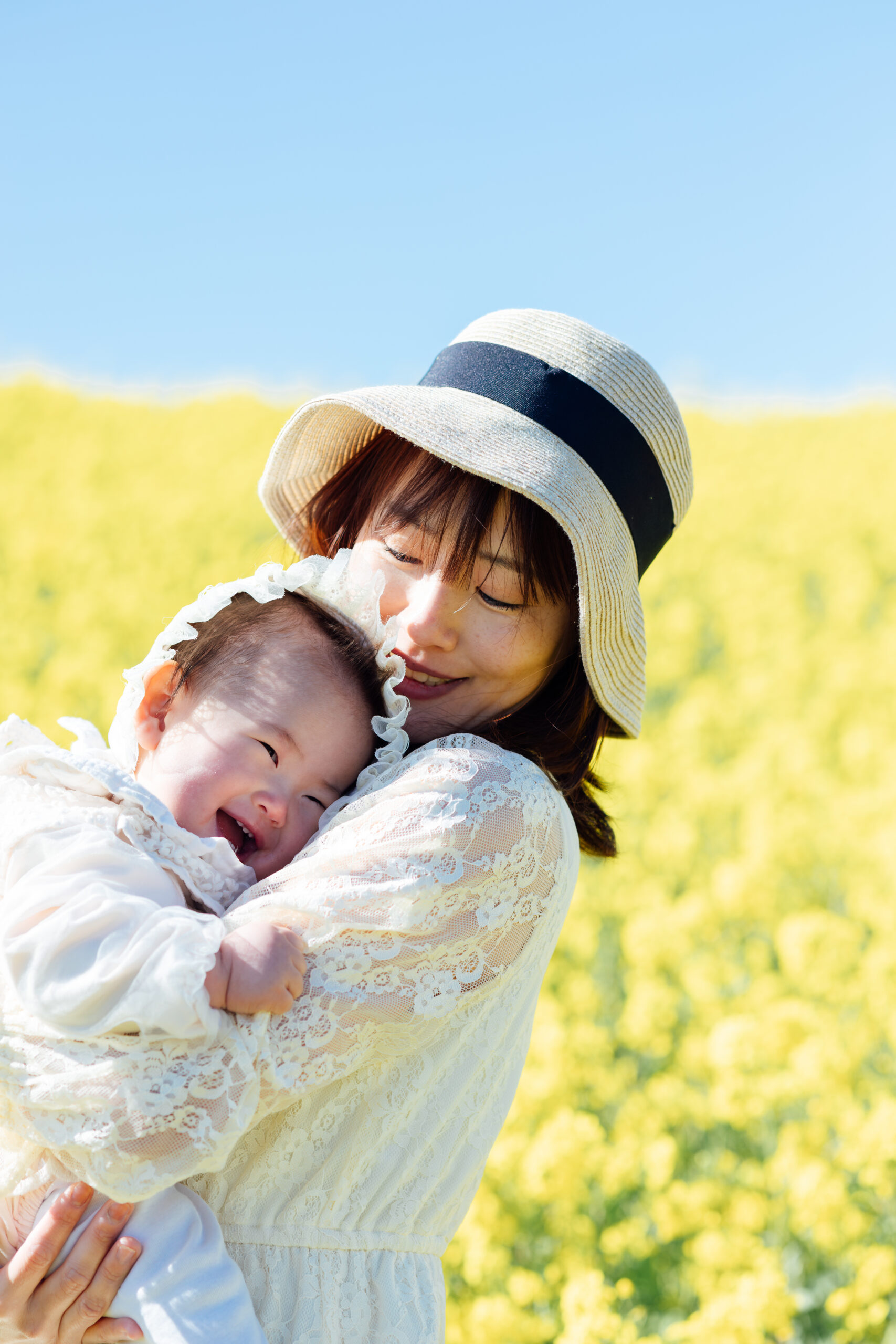 菜の花畑でお母さまに抱かれて笑う赤ちゃん