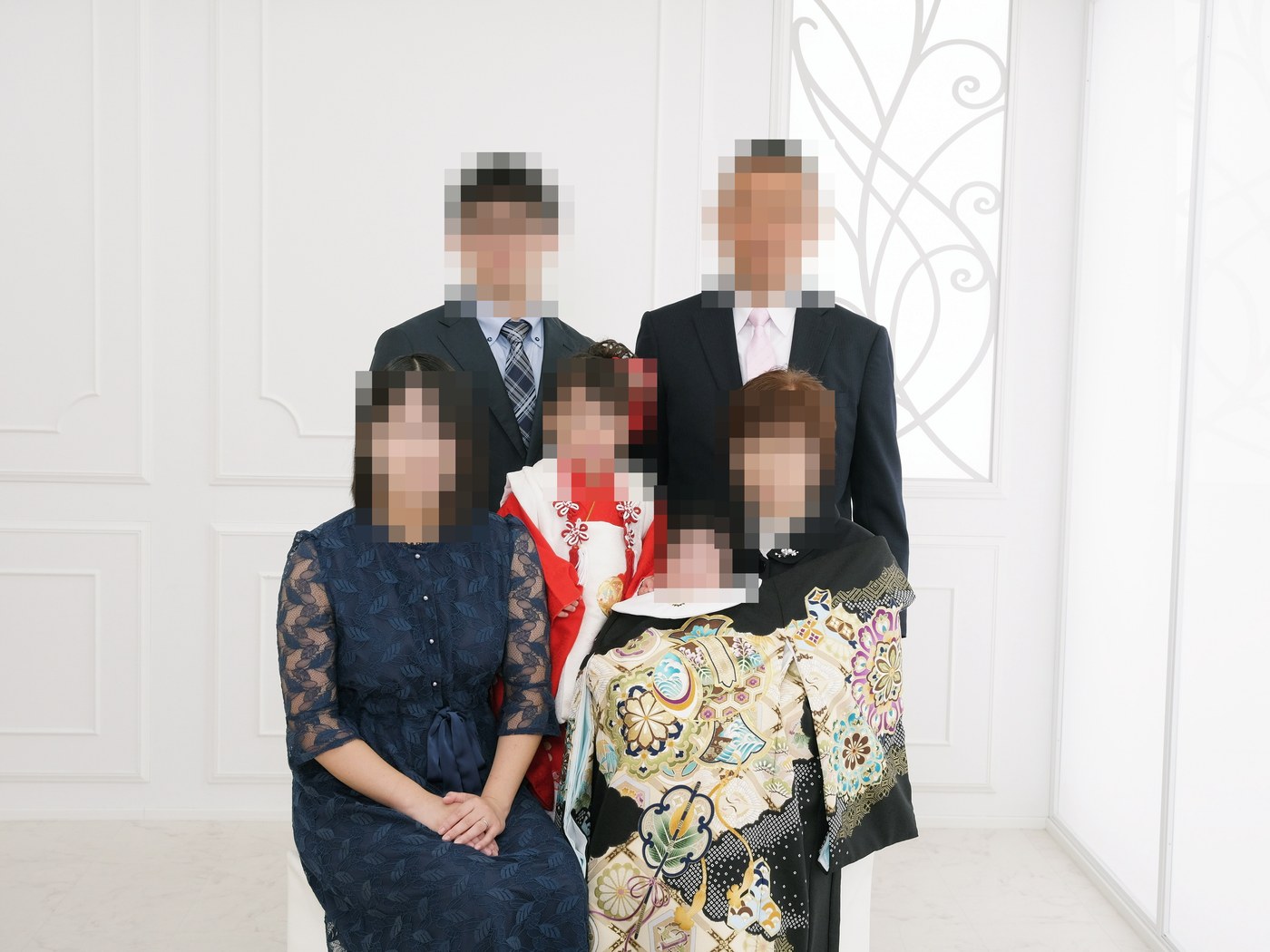 紺のレースワンピースを着た母親と、赤い着物の3歳の女の子、祝い着の赤ちゃん、スーツの父親、黒留袖と喪服の祖父母